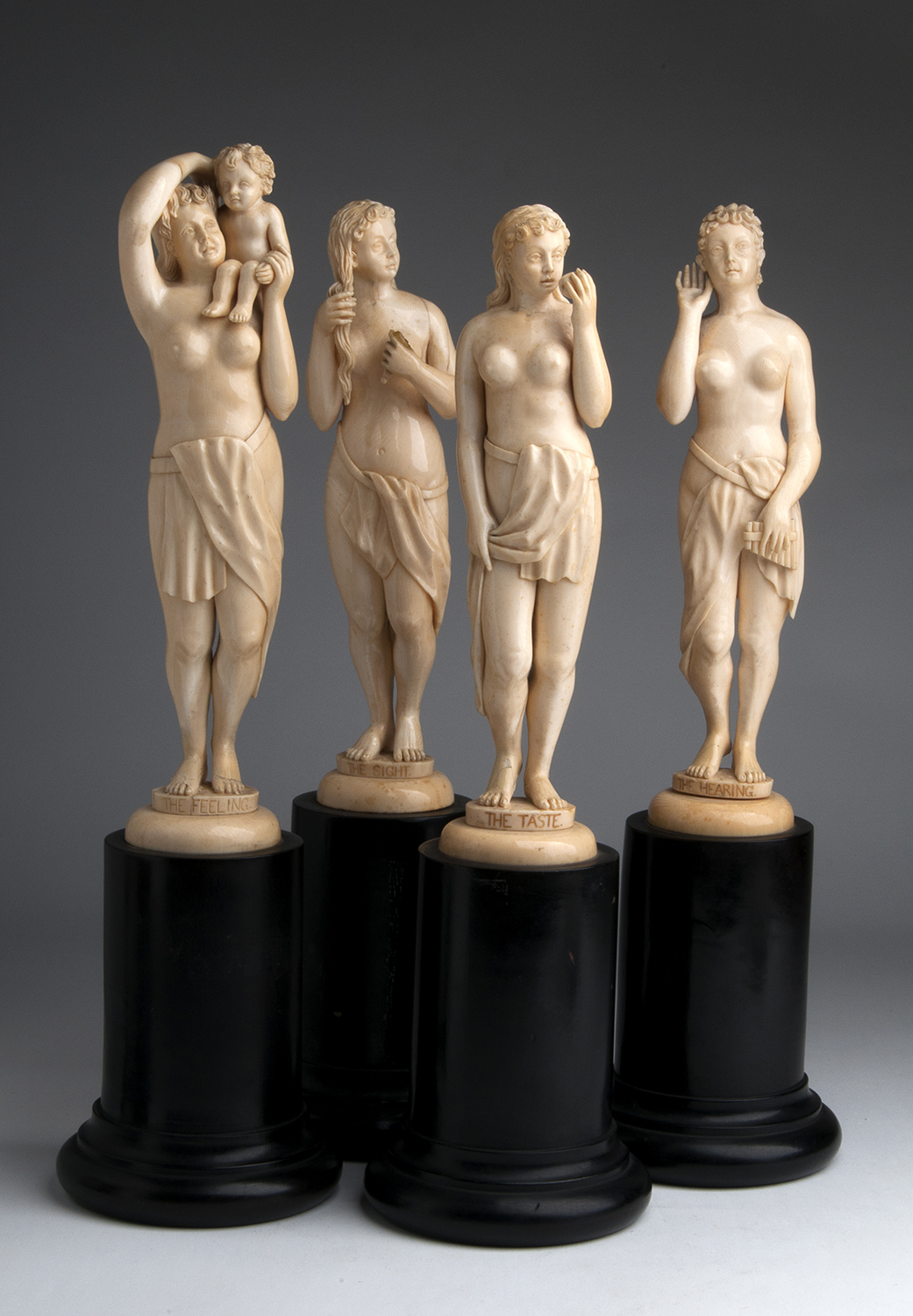 A carved ivory group of four female figures depicting "The Sight", "The Hearing", "The Taste" and "