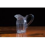 A 19TH CENTURY CUT GLASS JUG, with fluted rim and C-scroll handles cut with bold pillar flutes. 21cm