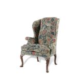 A GEORGE II WALNUT WINGBACK ARMCHAIR, now covered in crewel-pattern tapestry on lappeted cabriole