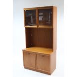 A teak-finish tall cabinet, the upper part enclosed by pair of glazed doors above an open shelf &
