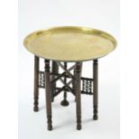 An Indian brass engraved circular tray-to occasional table on fold-away hardwood stand, 22¾” diam.