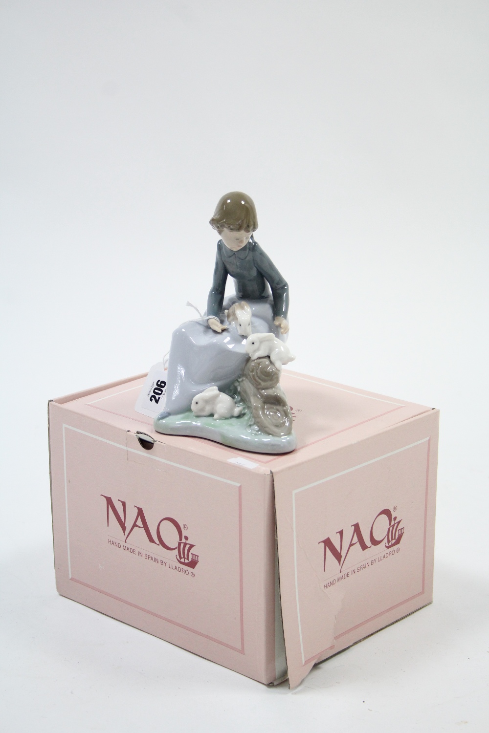 A Lladro Nao porcelain ornament in the form of a young girl seated on a log with three rabbits by