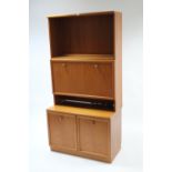 A teak-finish tall cabinet, the upper part enclosed by fall-front to centre with open recess above &