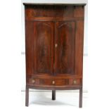 An early 19th century figured mahogany bow-front corner cupboard enclosed by a pair of fielded panel