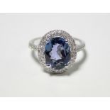 A TANZANITE RING, the oval cut stone approx. 3.7 carats set within a border of small diamonds, to