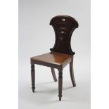 A Victorian mahogany hall chair with carved & shaped back, hard seat & on turned tapered legs.