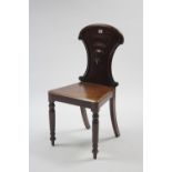 A Victorian mahogany hall chair with carved & shaped back, hard seat & on turned tapered legs.