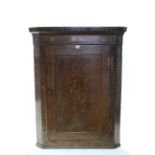 A late 18th century inlaid oak hanging corner cupboard fitted three shaped shelves enclosed by a