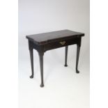 A mid-18th century "red walnut" tea table, the fold-over top with shaped corners, fitted frieze