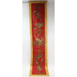 A Chinese silk scroll decorated in gold thread with lion dogs & peacocks on a red ground with flower