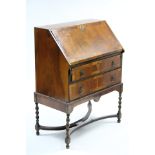 A reproduction small walnut bureau with fitted interior enclosed by fall-front above two long