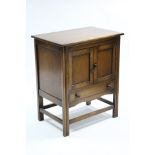 A reproduction oak dwarf cupboard enclosed by pair of panel doors above a long drawer, & on fluted