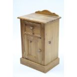 A pine bedside cabinet fitted frieze drawer above cupboard enclosed by panel door, and on plinth