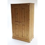 A pine small wardrobe fitted three shelves enclosed y pair of fielded panel doors & on plinth