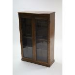 A mid-20th century oak standing bookcase with three adjustable shelves enclosed by pair of leaded