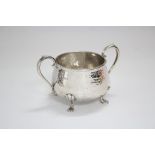 A squat round two-handled sugar bowl with all-over planished surface, on four paw feet, 5½” wide (