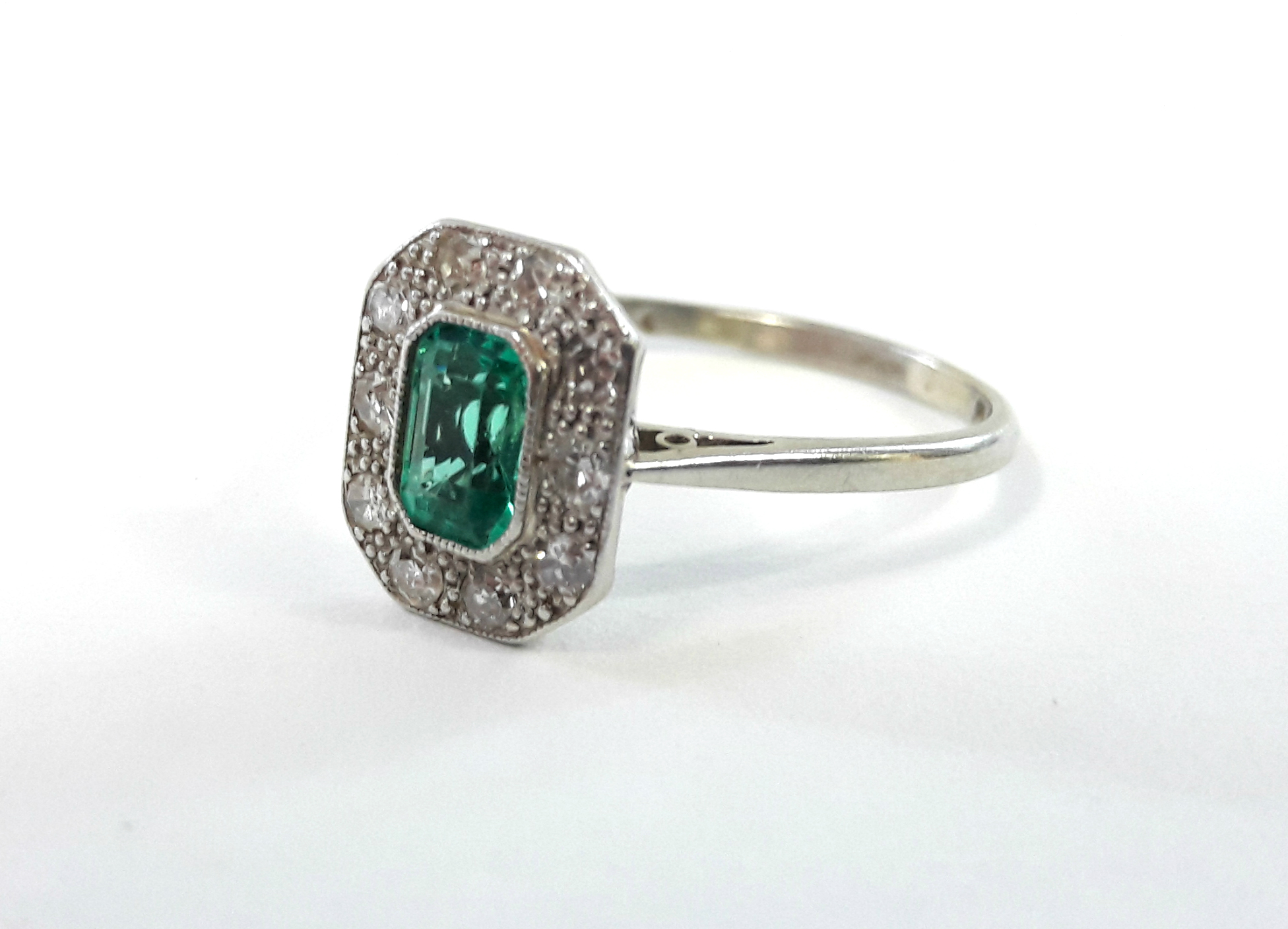 A platinum ring set rectangular emerald within a border of ten small diamonds.