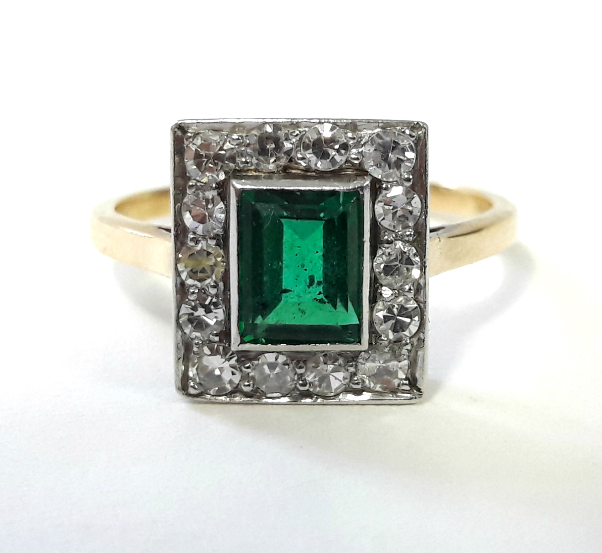 AN EMERALD & DIAMOND RING, the centre rectangular emerald set within a border of fourteen small