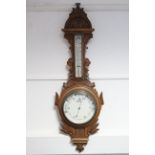 A late 19th/early 20th century aneroid wall barometer with white enamel dial, and in carved oak