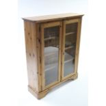 A Ducal pine standing cabinet, fitted three plate-glass shelves enclosed by pair of glazed doors &