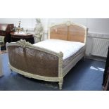 A late 19th/early 20th century French carved & painted double bedstead with rounded cane-panel