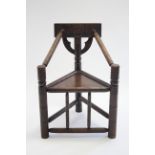 An oak turner’s chair with triangular seat & primitive carved decoration to the back, bears label to