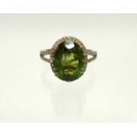 A PERIDOT RING, the oval stone of approx. 5.7 carats, set within a border of small diamonds to a