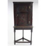 An 18th century oak hanging corner cupboard enclosed by a carved panel door, on later stand with