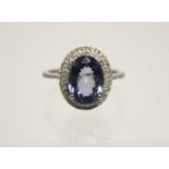 A TANZANITE RING, the oval stone of approx. 3.5 carats set within a border of small diamonds to a