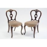 A pair of mid-Victorian rosewood dining chairs with carved open rounded backs, shaped padded