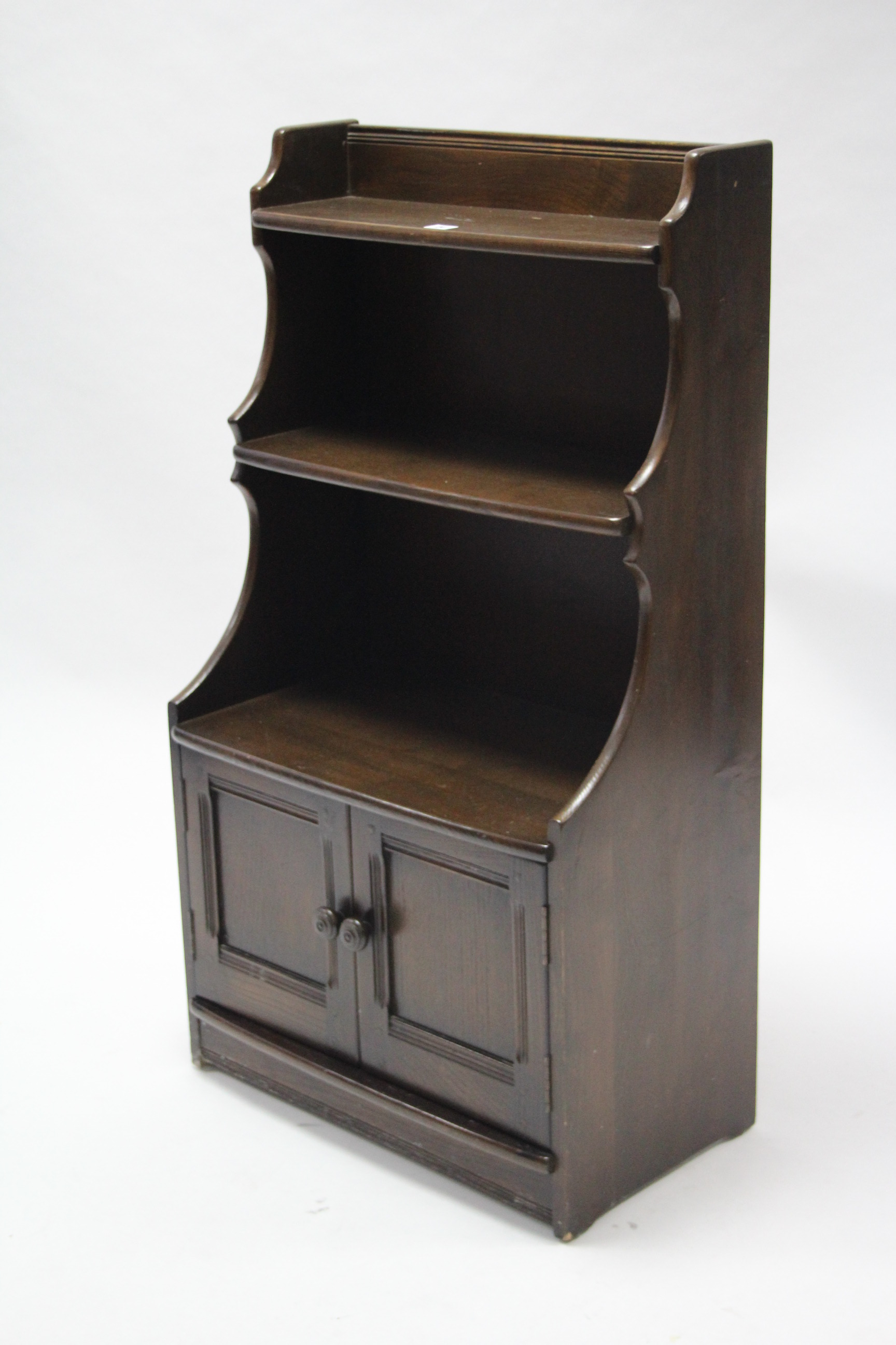 An Ercol dark elm small standing cabinet fitted two open shelves above cupboard enclosed by pair