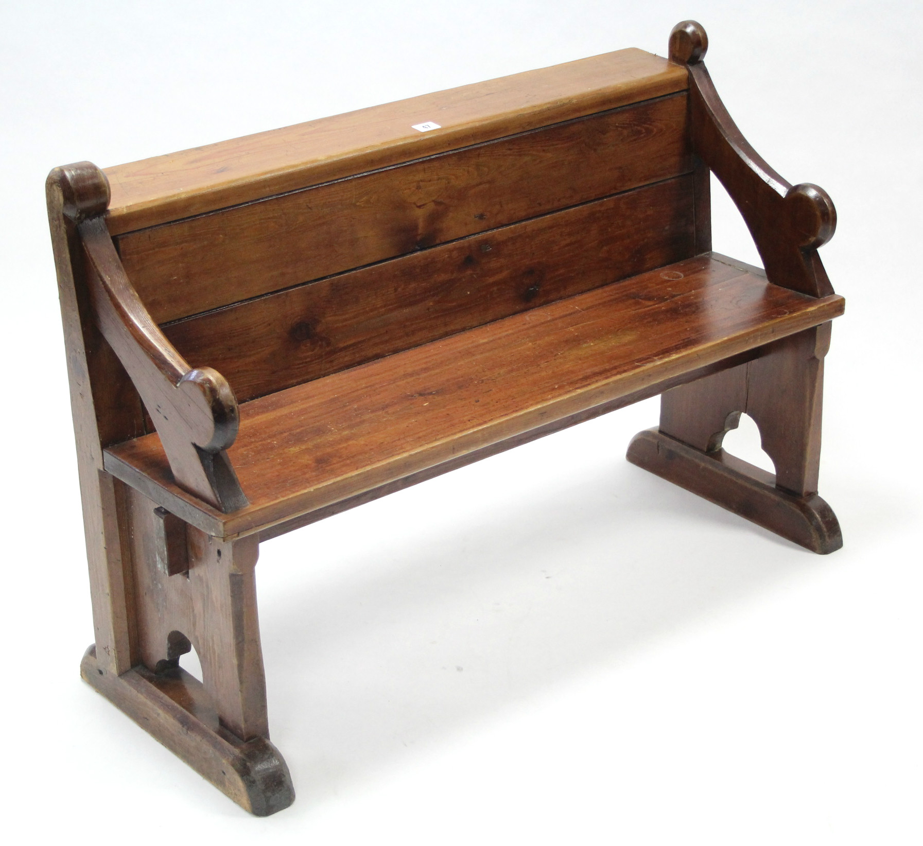 A child's pitch pine settle with panelled back, hard seat, & on shaped end supports, 39" long.