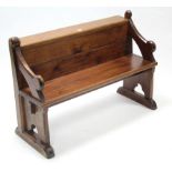 A child's pitch pine settle with panelled back, hard seat, & on shaped end supports, 39" long.