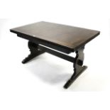 An Ercol dark elm draw-leaf dining table on shaped end supports, joined by plain centre stretcher,