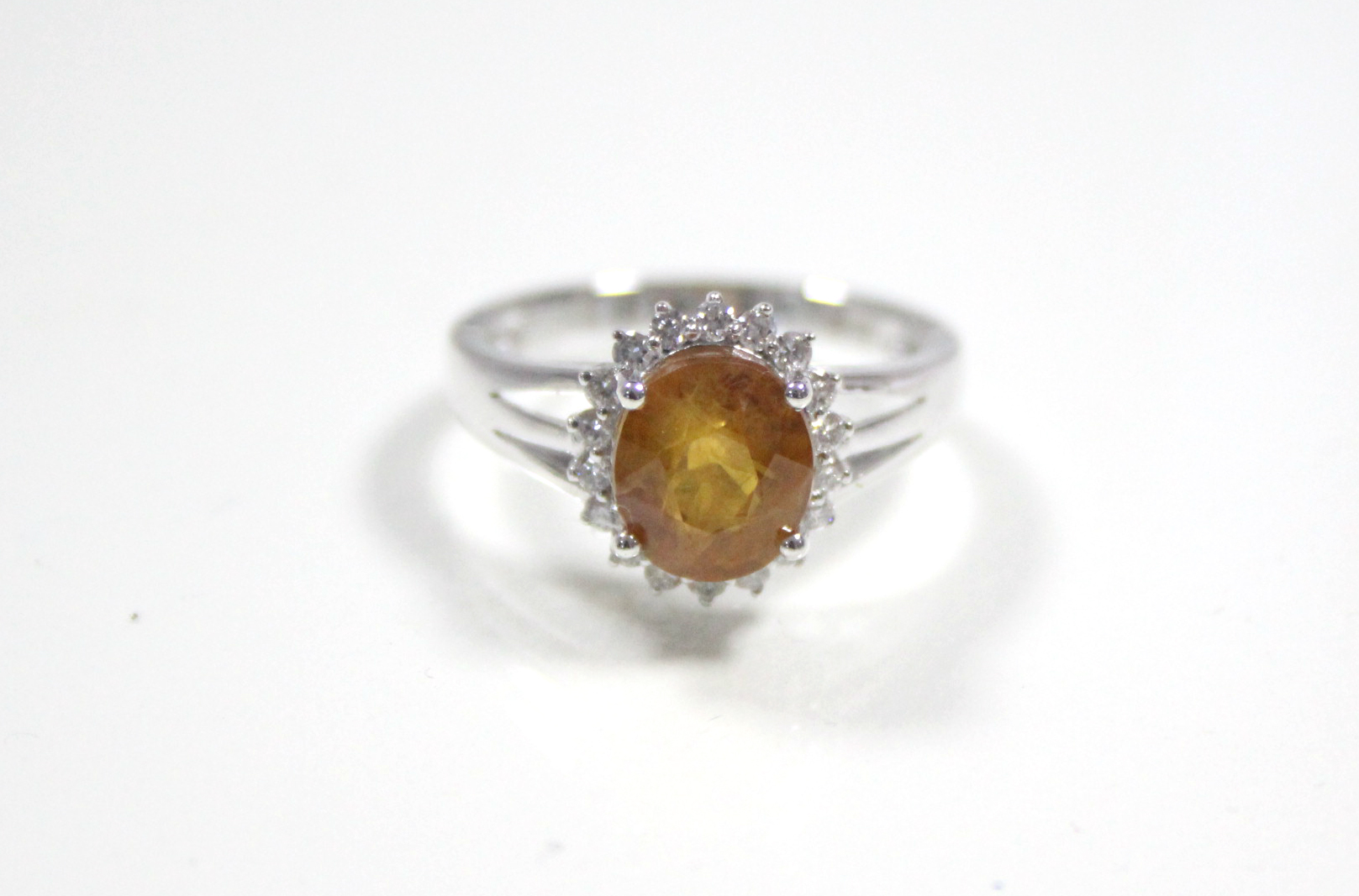 A white 14K ring set yellow-orange oval-cut sapphire within a boarder of small diamonds.