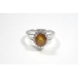 A white 14K ring set yellow-orange oval-cut sapphire within a boarder of small diamonds.