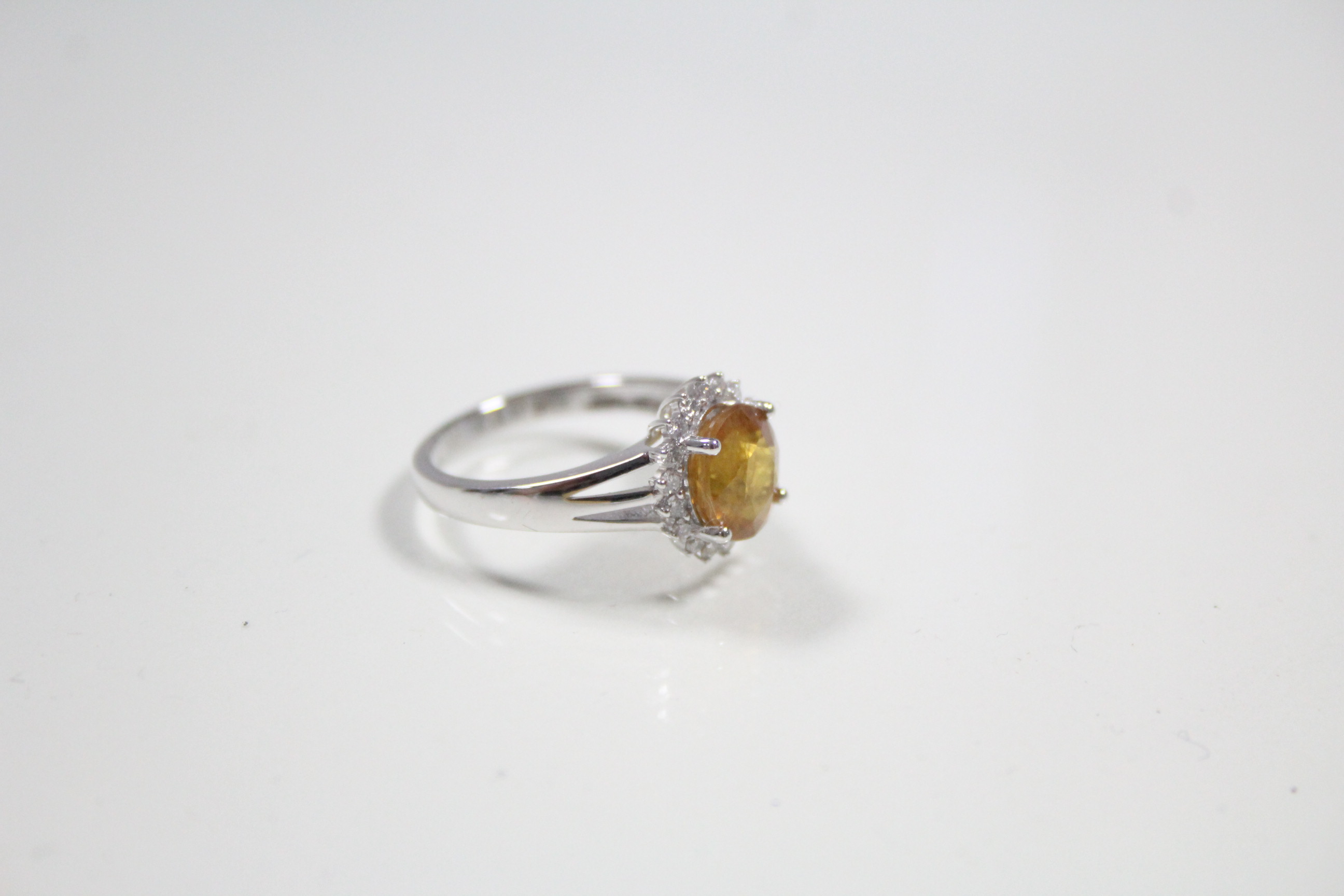 A white 14K ring set yellow-orange oval-cut sapphire within a boarder of small diamonds. - Image 2 of 3