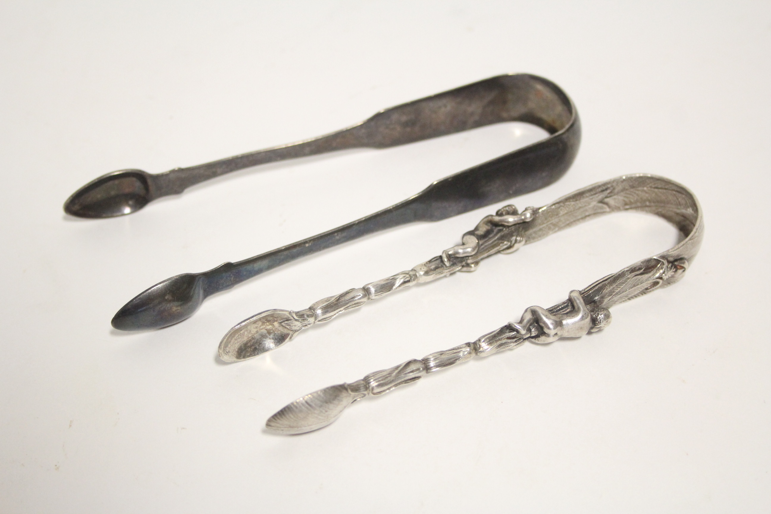 A pair of Victorian “Banana Palm” sugar tongs, each cast stem with a figure climbing up the trunk,