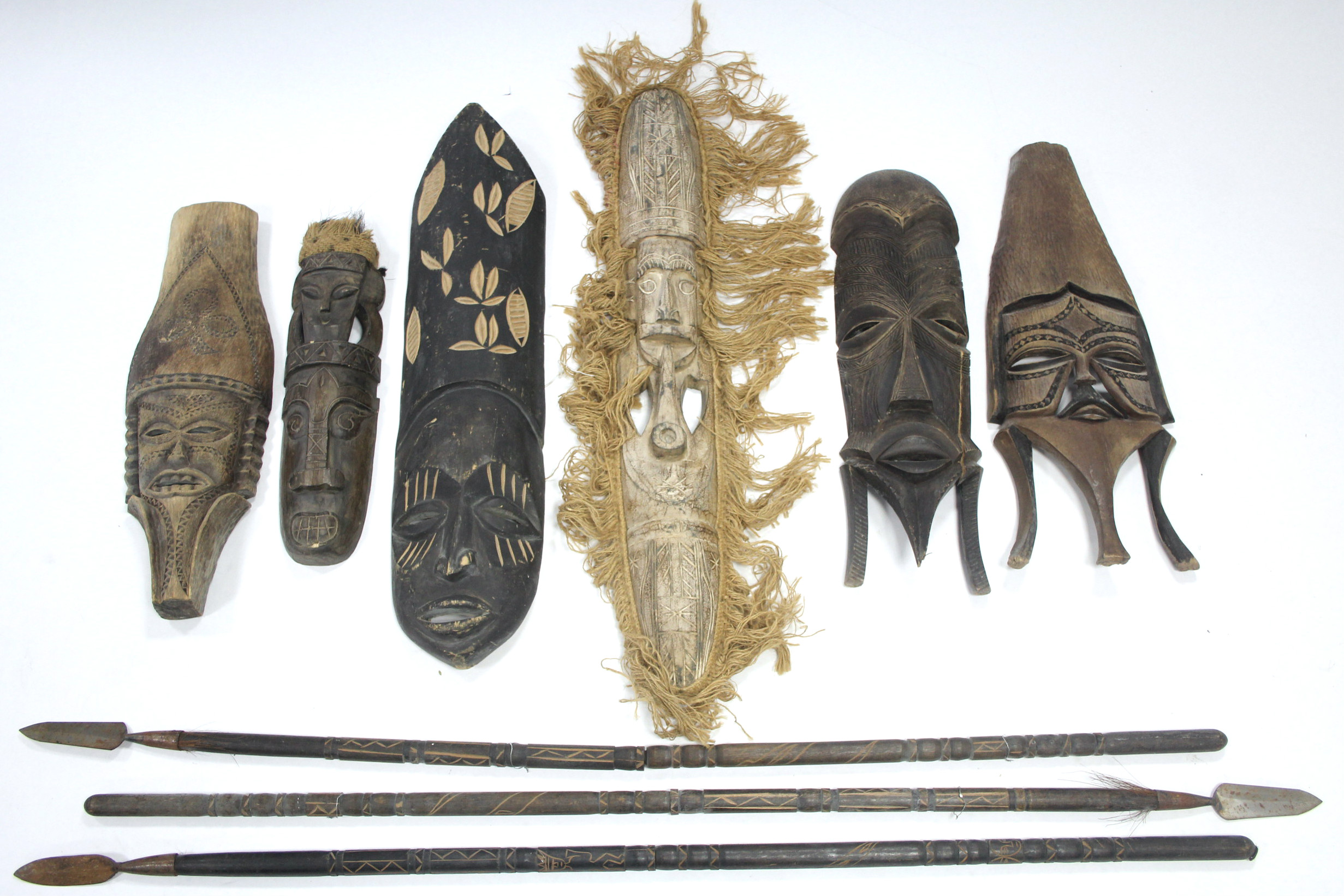 A collection of African artefacts including carved wood masks, spears, bows & arrows, fly-whisks,