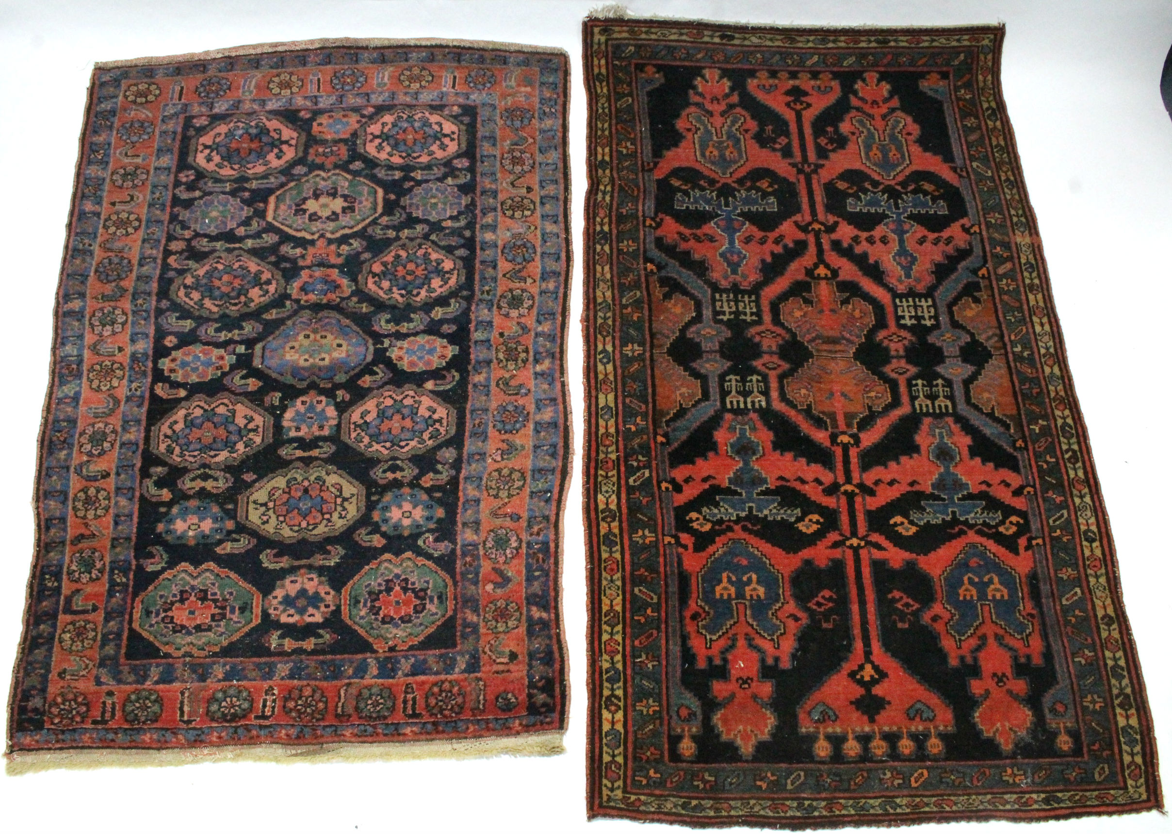 A Persian rug of dark blue ground, pink, blue, & ivory figured with abstract motifs within narrow