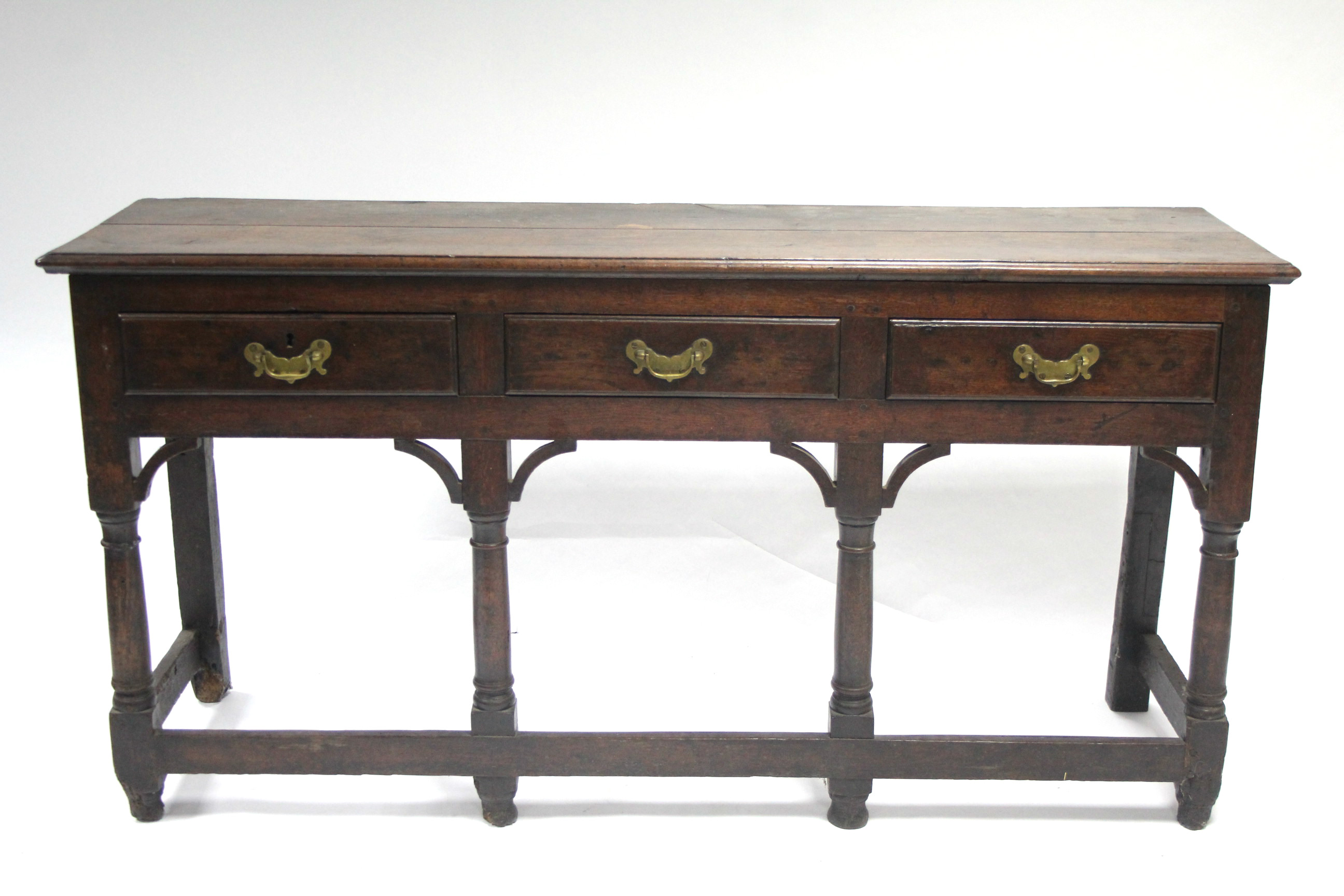 AN 18th century OAK DRESSER BASE, fitted three drawers with shaped brass handles, & on turned