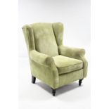 A modern wing-back armchair upholstered pale green velour, & on short turned legs.
