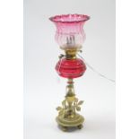 A brass oil table lamp (converted to electricity) on shaped centre column, with cranberry glass