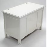 A white painted wooden blanket box with hinged lift-lid, panelled front, & on square supports,