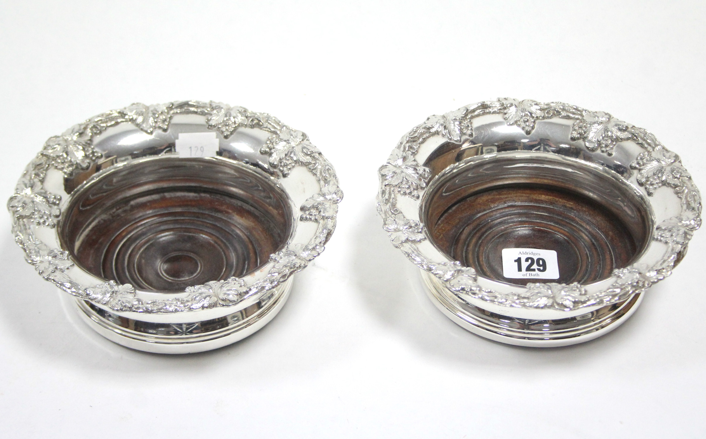 A pair of silver plated coasters with raised vine-leaf borders, & with carved treen bases, 6¾”