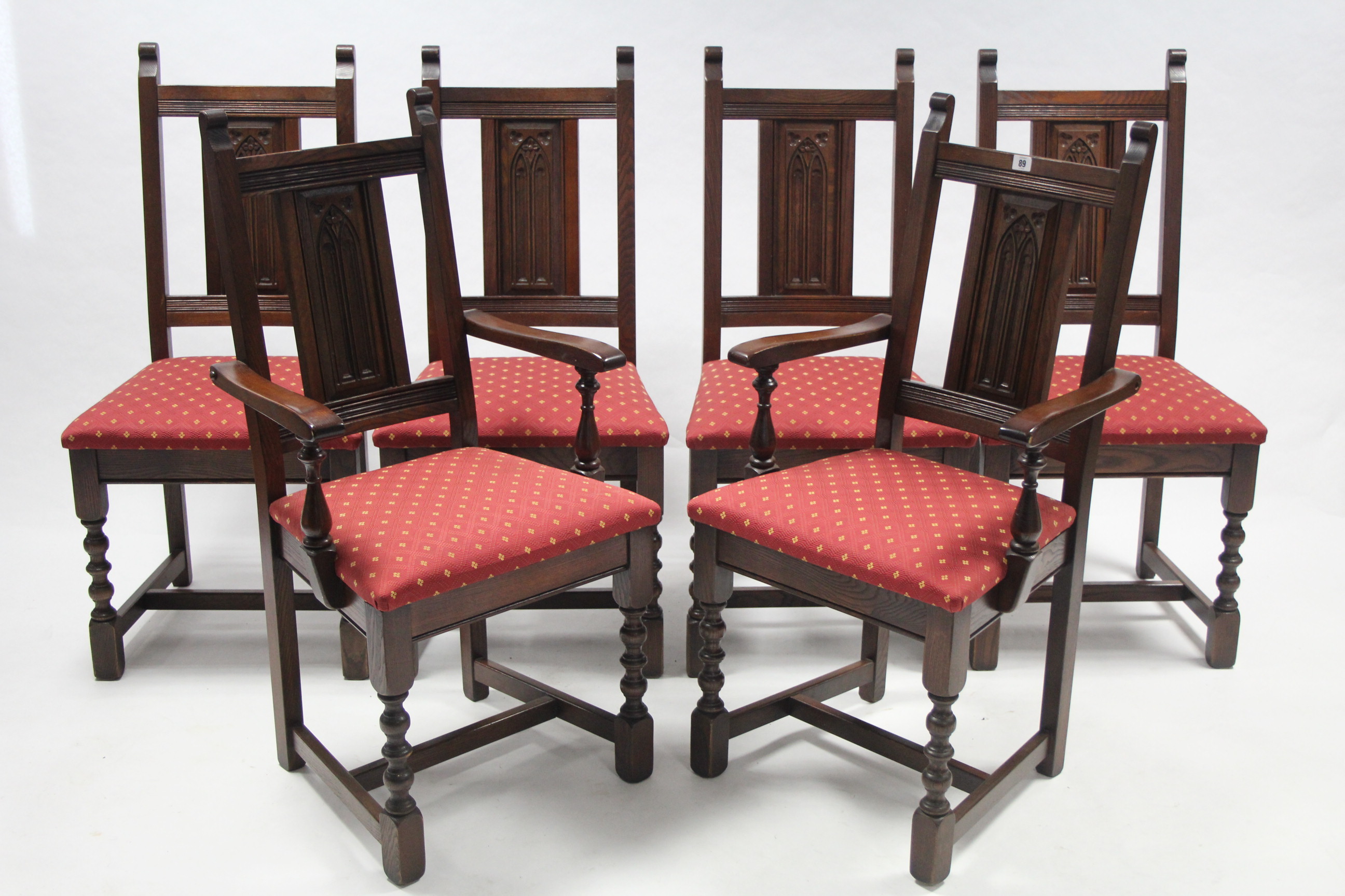 A set of six oak dining chairs (including a pair of carvers) with carved panel backs, padded