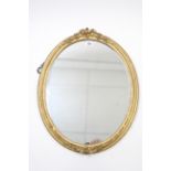 A gilt frame oval wall mirror with foliate surmount, 23” x 18½”.