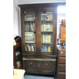 A 1920’s oak tall standing bookcase with three adjustable shelves enclosed by pair of leaded