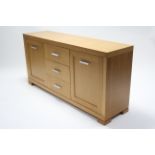 A light oak-finish sideboard fitted three long graduated drawers to centre with cupboard to either