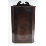 A late 18th century figured mahogany hanging corner cupboard with swan-neck pediment, marquetry